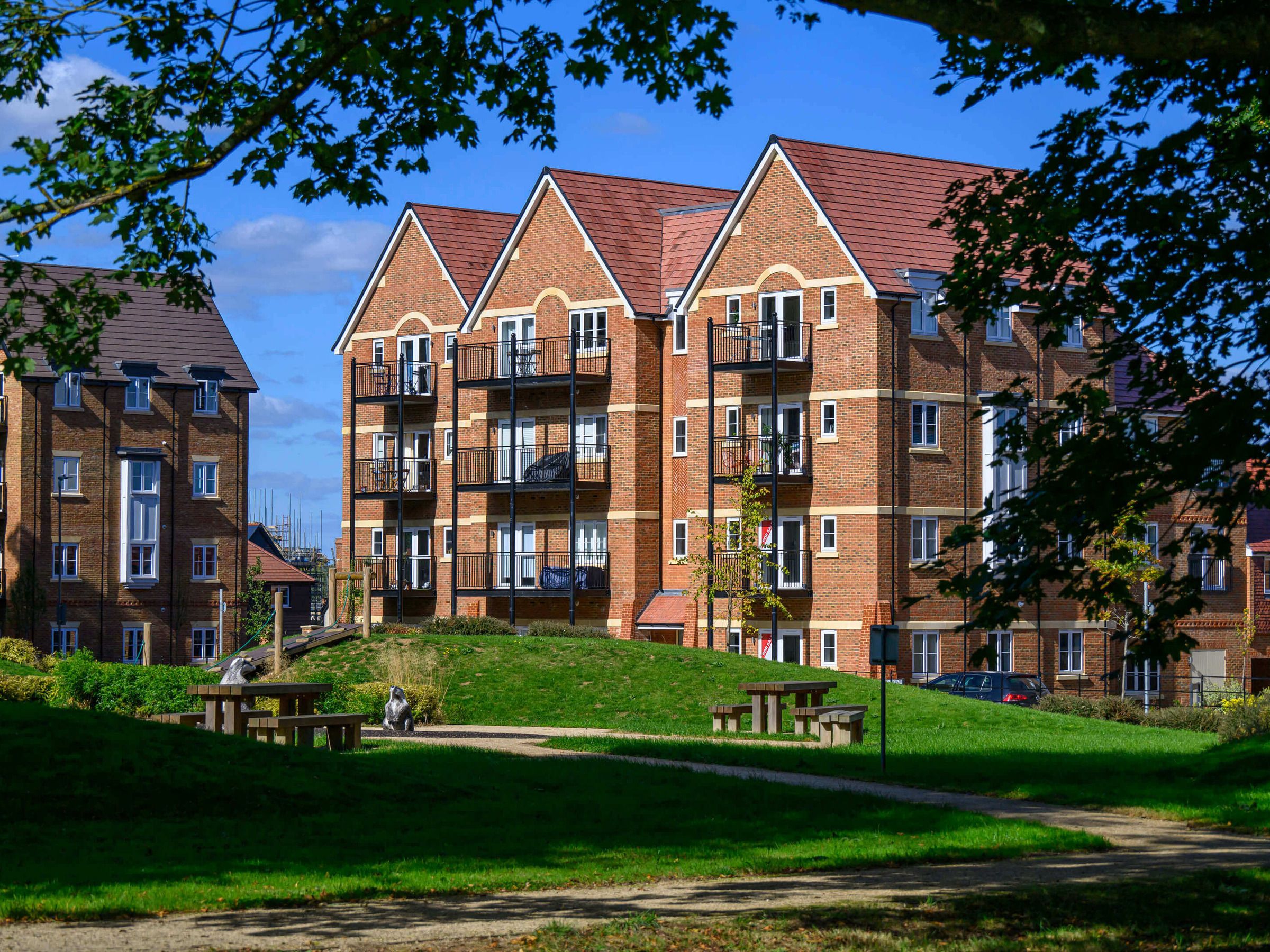 Apartment building in brick with balconies, lawn and trees in front